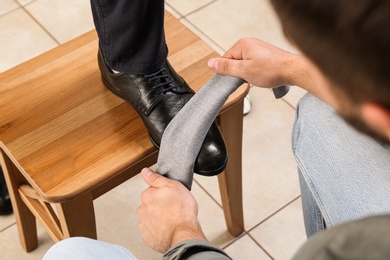 Man shining client's shoe on wooden stool indoors, closeup