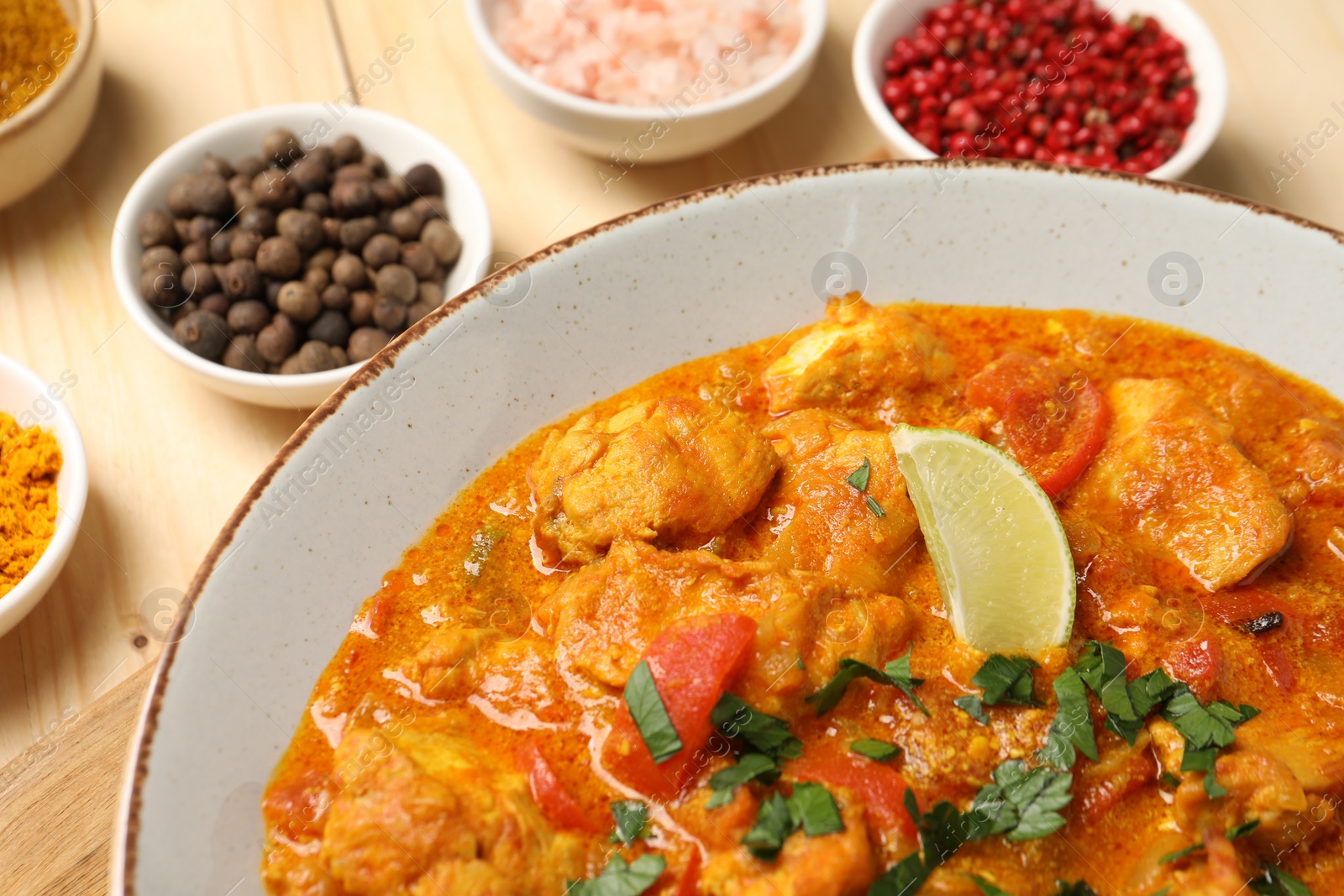 Photo of Delicious chicken curry and spices on wooden table, closeup