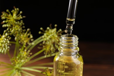 Photo of Dripping dill essential oil from pipette into bottle against black background, closeup