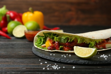 Delicious tortilla with meat on black table against wooden background