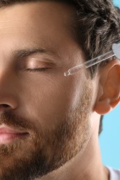 Photo of Handsome man applying cosmetic serum onto his face, closeup