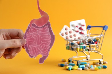 Woman holding paper intestine cutout near shopping cart with many pills on orange background, closeup