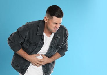 Photo of Man suffering from stomach ache on light blue background, space for text. Food poisoning