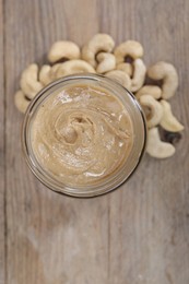 Photo of Tasty cashew nut paste in jar on wooden table, top view. Space for text