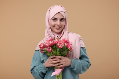 Happy woman in hijab with beautiful bouquet on beige background