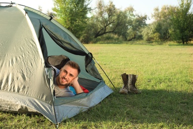 Young man lying inside camping tent on sunny day