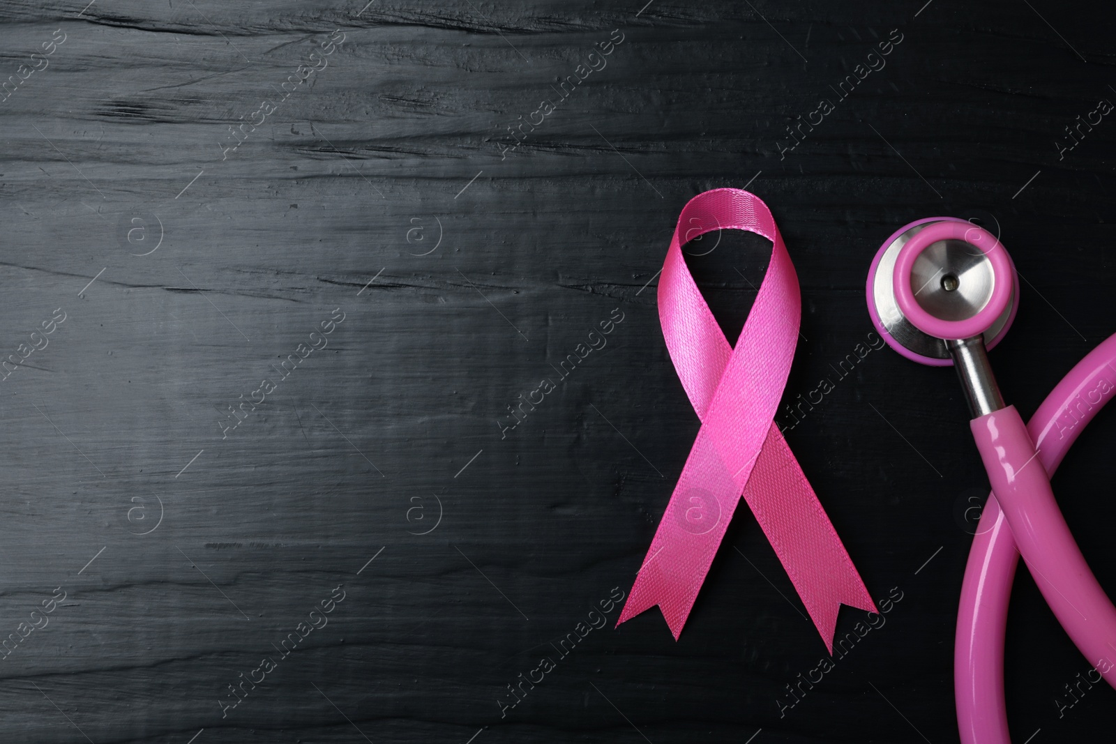 Photo of Pink ribbon and stethoscope on wooden background, top view with space for text. Breast cancer concept