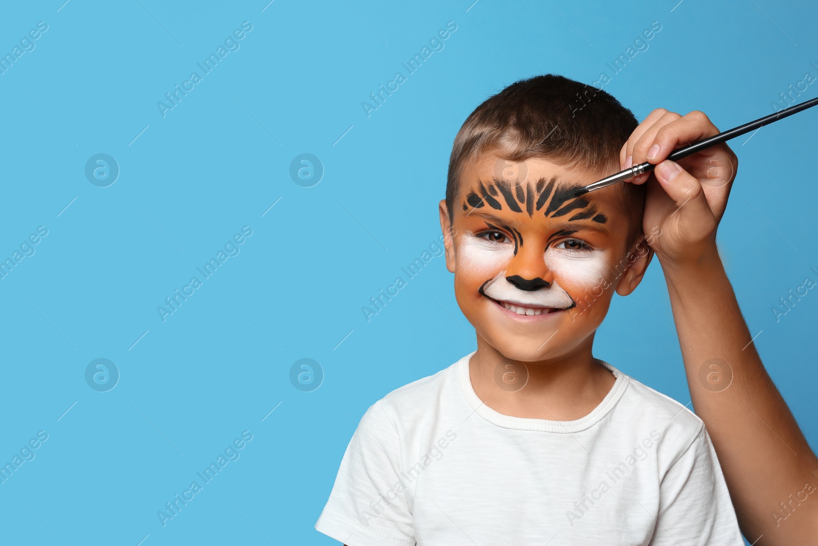 Photo of Artist painting face of little boy on blue background. Space for text