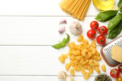 Different types of pasta, grater and products on white wooden table, flat lay. Space for text