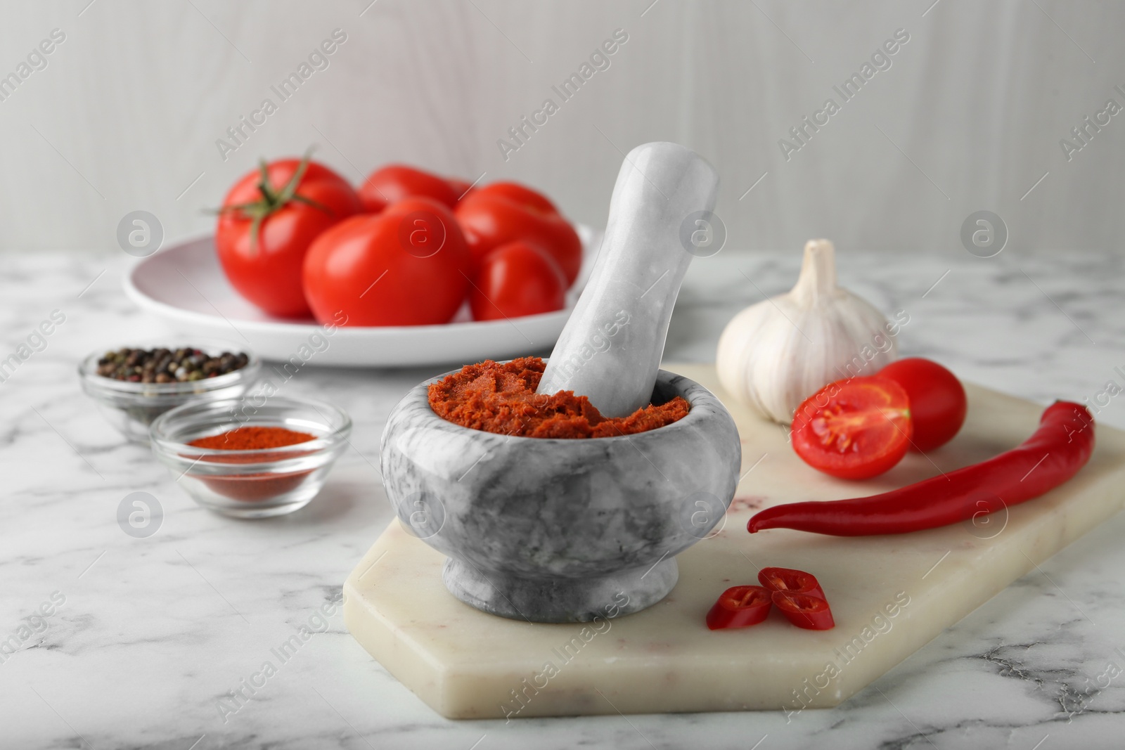 Photo of Red curry paste in mortar and ingredients on white marble table