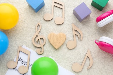 Photo of Wooden notes, music sheets, headphones and toys on beige textured background, flat lay. Baby song concept