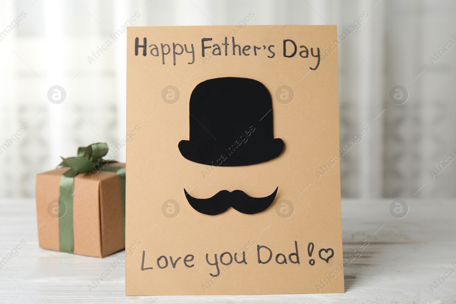 Photo of Greeting card with phrase HAPPY FATHER'S DAY I LOVE YOU DAD and gift box on white wooden table indoors