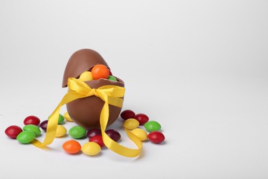 Photo of Tasty chocolate egg with yellow bow and colorful candies on light background. Space for text