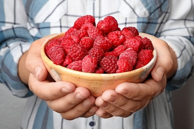Photo of Woman holding bowl with delicious ripe raspberries, closeup