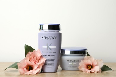 Photo of MYKOLAIV, UKRAINE - SEPTEMBER 07, 2021: Kerastase hair care cosmetic products and beautiful flowers on wooden table