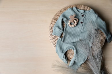 Photo of Baby bodysuit, toy and feather on wooden background, flat lay. Space for text