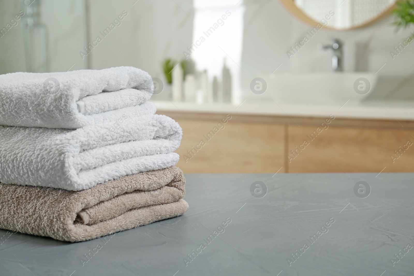 Photo of Stack of clean towels on grey stone table in bathroom. Space for text