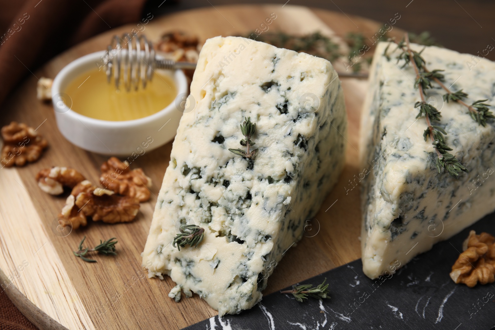 Photo of Tasty blue cheese with thyme, honey and walnuts on wooden board, closeup