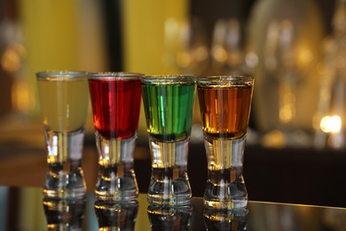 Photo of Different shooters in shot glasses on mirror surface against blurred background. Alcohol drink