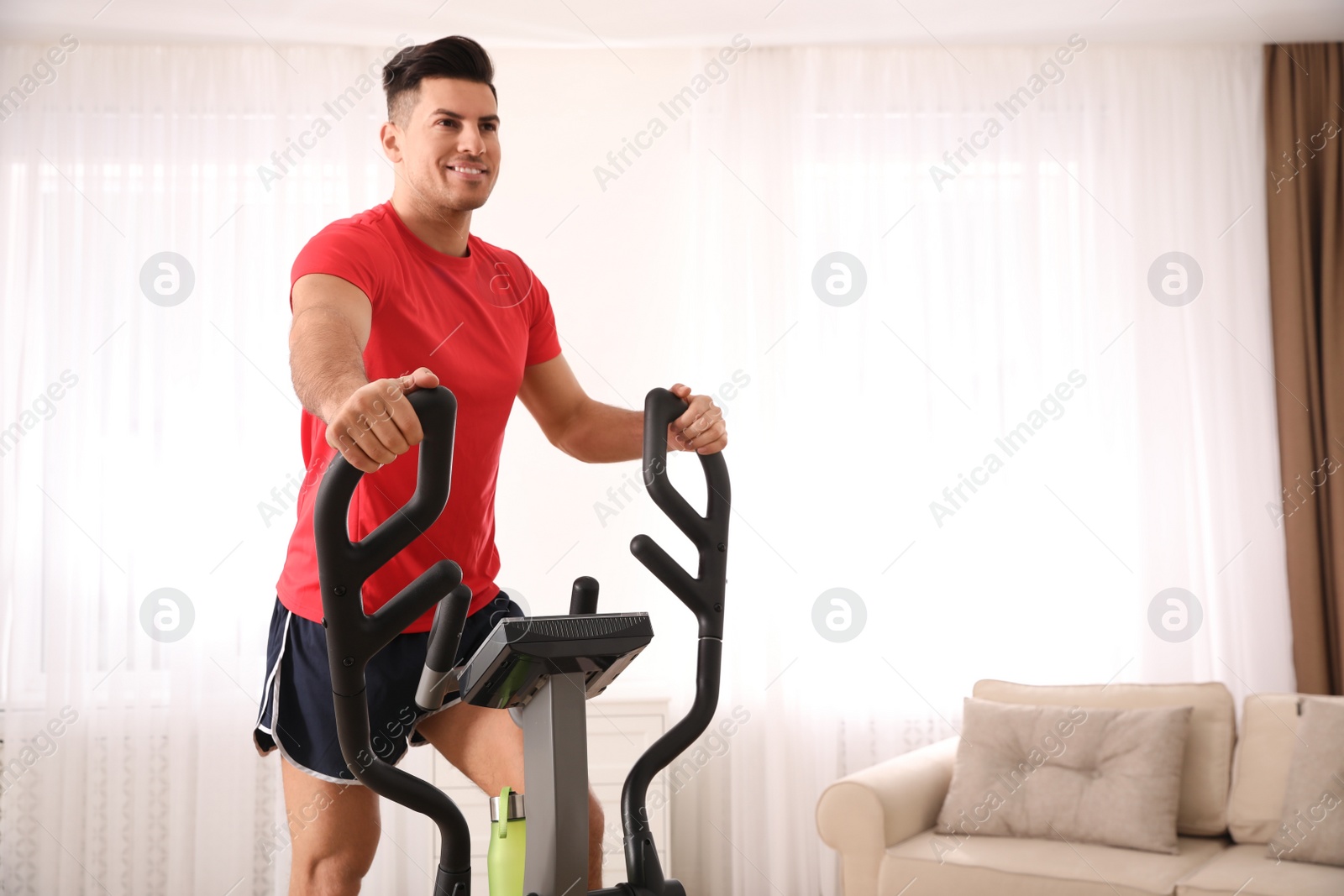 Photo of Man using modern elliptical machine at home