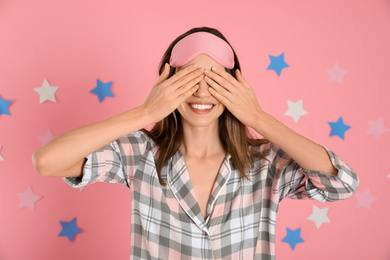 Photo of Beautiful woman wearing pajamas and sleep mask on pink background. Bedtime