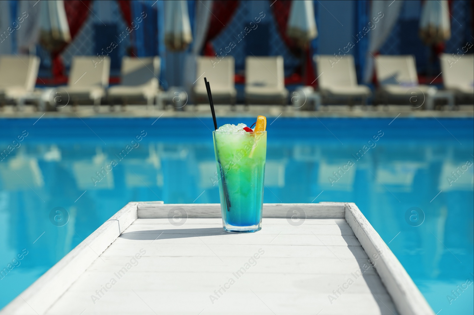 Photo of Refreshing cocktail on wooden table near swimming pool outdoors