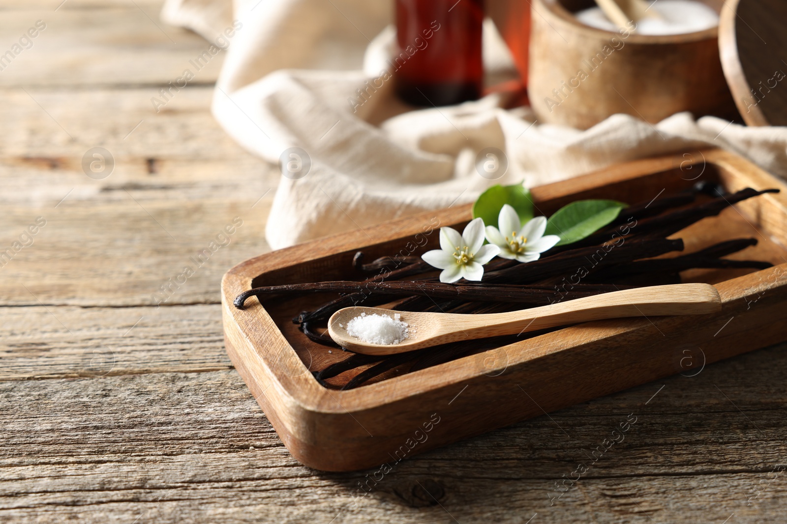 Photo of Vanilla pods, flowers, leaves and spoon with sugar on wooden table, closeup. Space for text