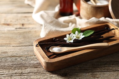 Vanilla pods, flowers, leaves and spoon with sugar on wooden table, closeup. Space for text