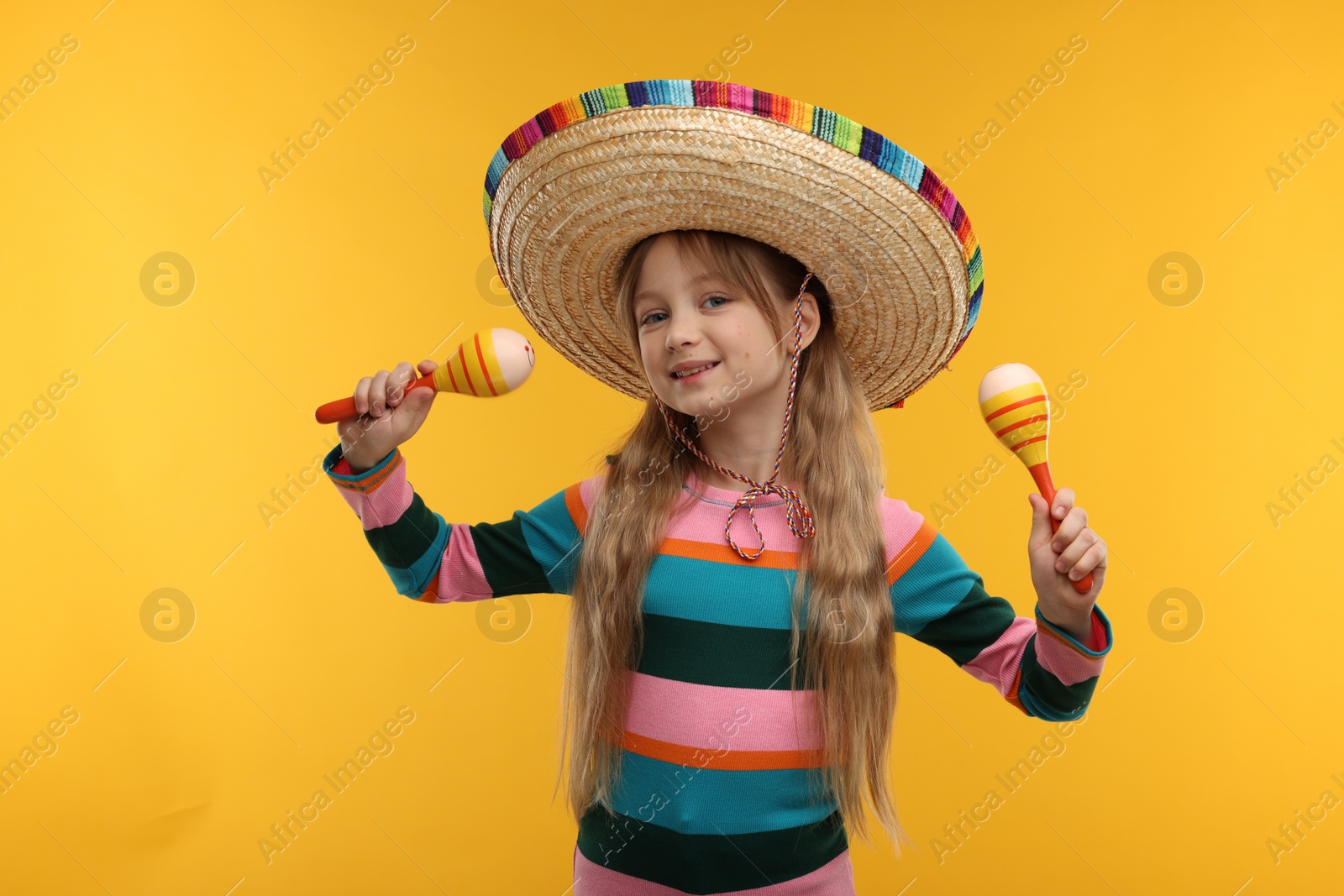 Photo of Cute girl in Mexican sombrero hat dancing with maracas on orange background