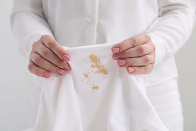 Photo of Woman holding shirt with stain against light background, closeup
