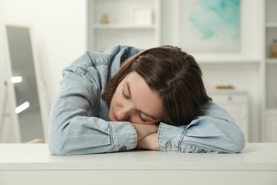 Sad young woman sitting at white table in room