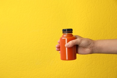 Photo of Woman holding bottle of carrot juice on color background, closeup with space for text