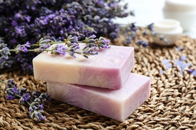 Photo of Handmade soap bars with lavender flowers on wicker mat, closeup