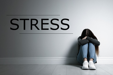 Word STRESS and depressed young girl sitting on floor indoors