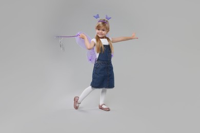 Cute little girl in fairy costume with violet wings and magic wand on light grey background
