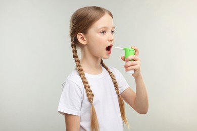 Little girl using throat spray on light grey background