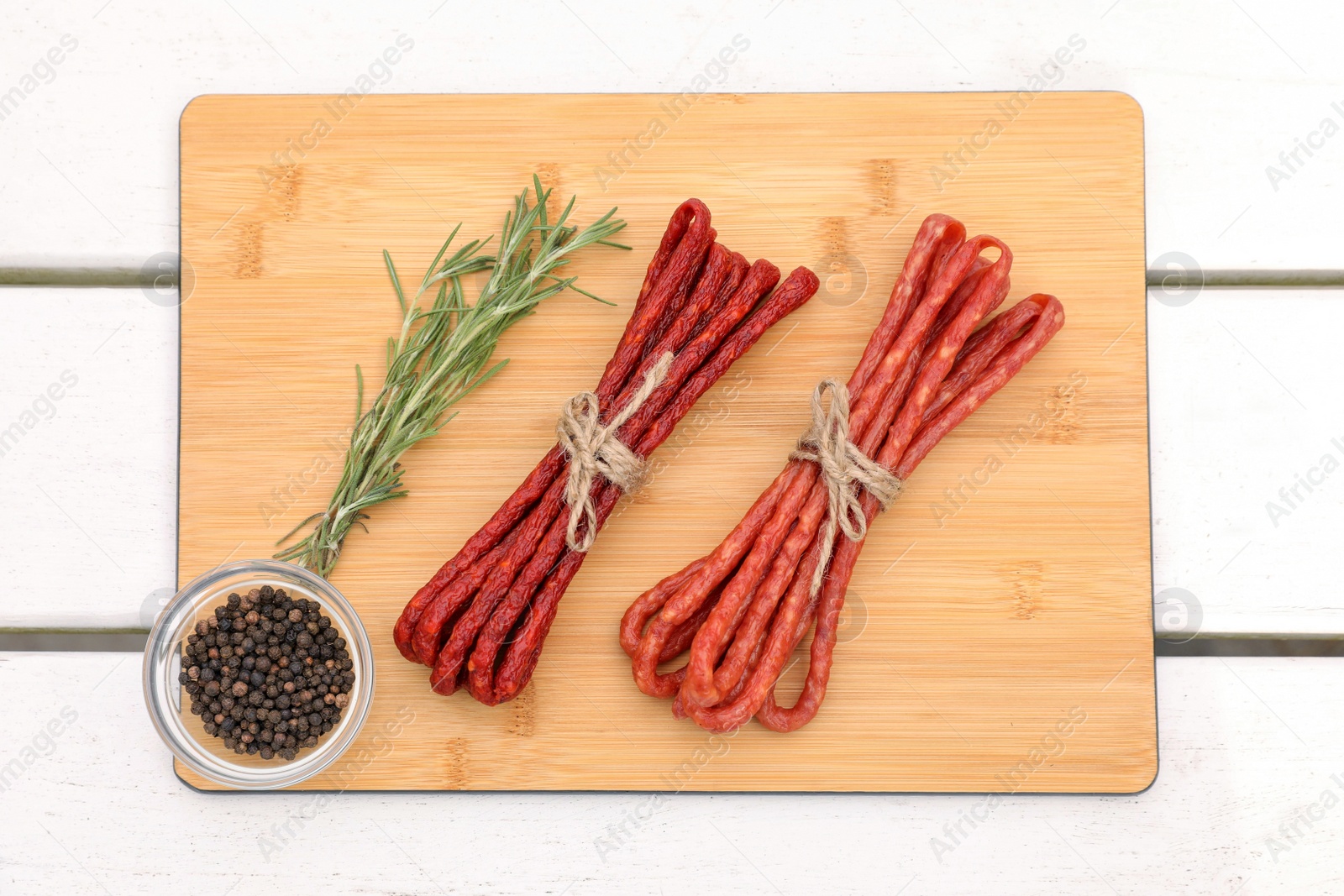 Photo of Bundles of delicious kabanosy with peppercorn and rosemary on white wooden table, top view