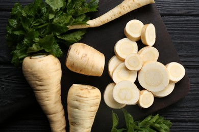 Whole and cut parsnips on black wooden table, flat lay