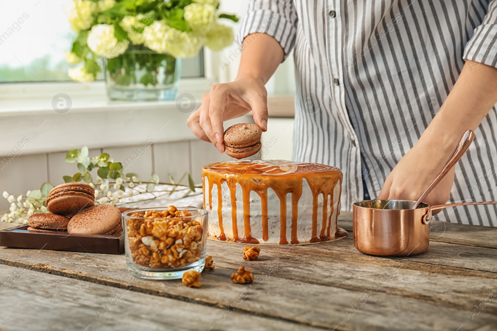 Photo of Young woman decorating delicious caramel cake at table