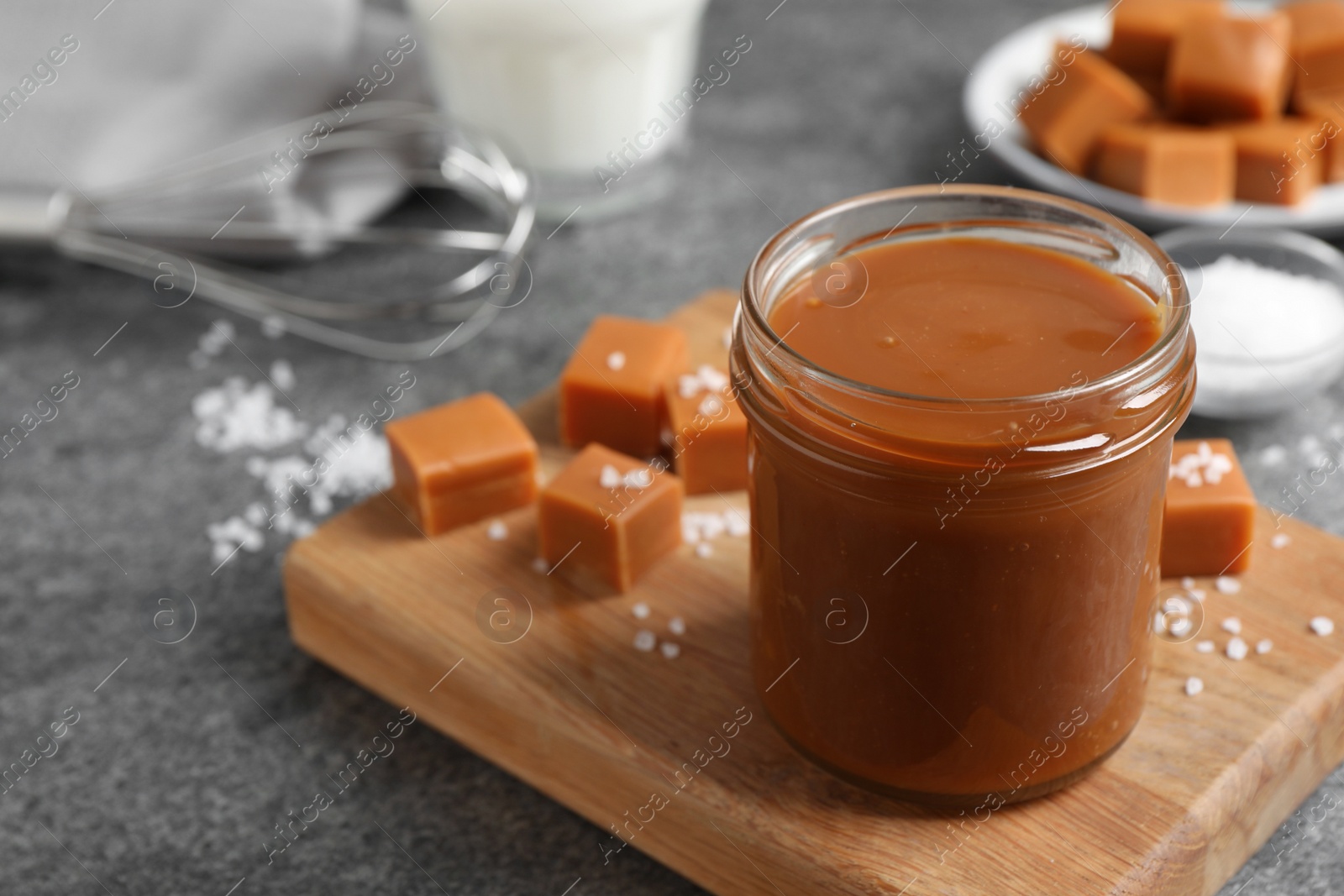 Photo of Yummy salted caramel in glass jar and candies on grey table, space for text