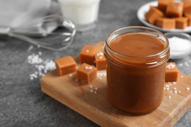 Yummy salted caramel in glass jar and candies on grey table, space for text