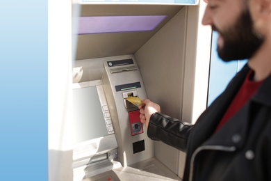 Man inserting credit card into cash machine outdoors, closeup