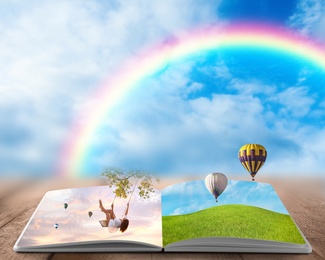 Image of Fantasy worlds in fairytales. Book, hot air balloons and rainbow in cloudy blue sky on background