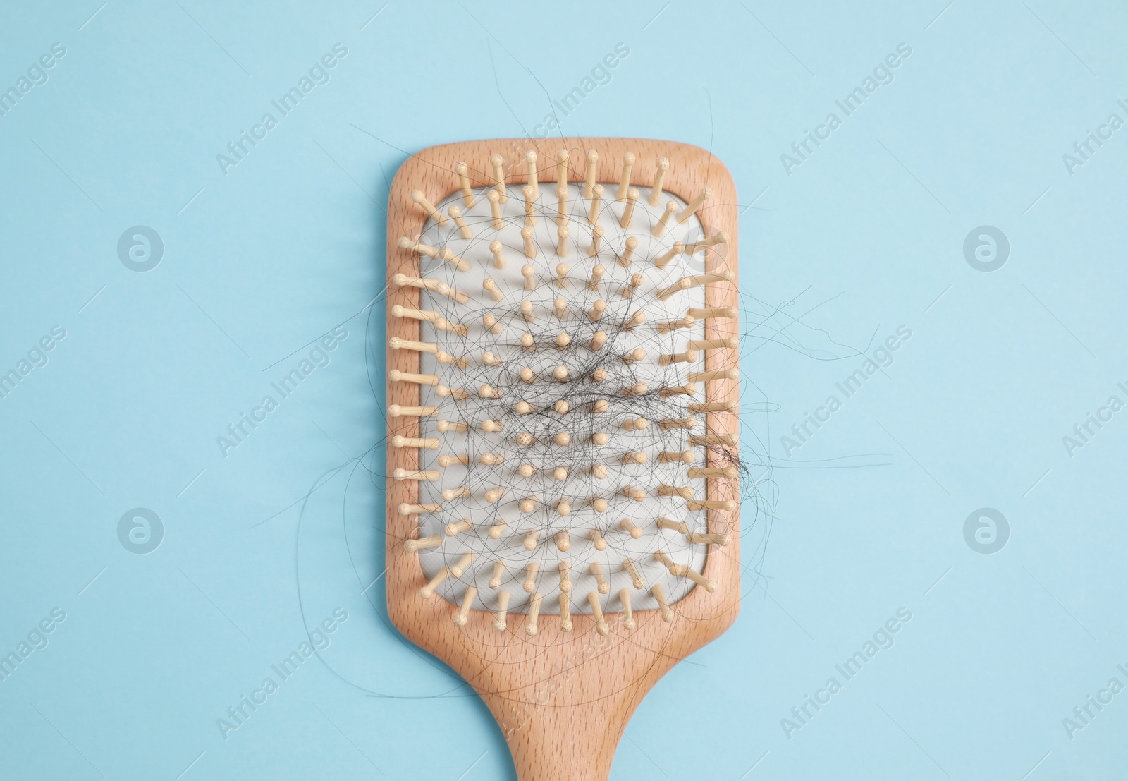 Photo of Wooden brush with lost hair on light blue background, top view