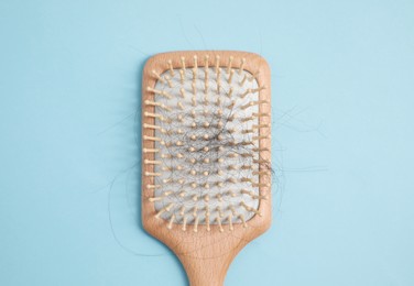 Wooden brush with lost hair on light blue background, top view