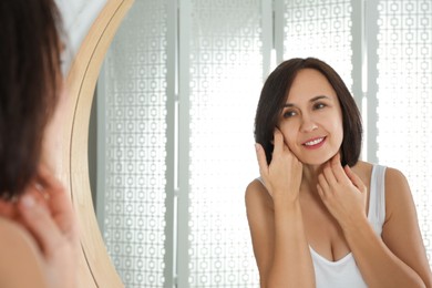 Happy mature woman with clean skin looking at mirror in bathroom