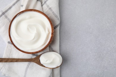 Photo of Delicious natural yogurt in bowl and spoon on light grey table, top view. Space for text