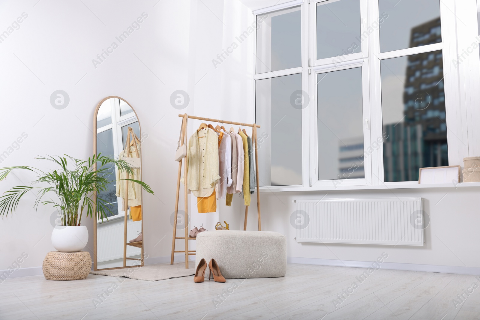 Photo of Stylish dressing room interior with mirror, ottoman and clothing rack