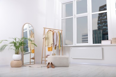Photo of Stylish dressing room interior with mirror, ottoman and clothing rack