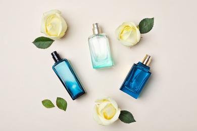 Bottles of perfume and roses on light background, top view